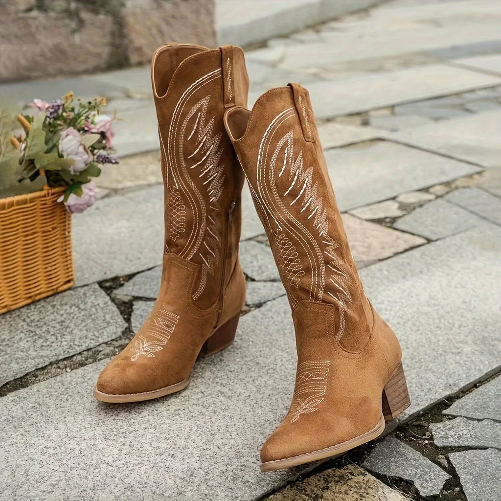 Pair of camel suede knee-high boots with pointed toe and stacked block heel, standing on cobblestones