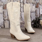 Pair of ivory white embroidered cowboy boots standing side by side against a stone wall