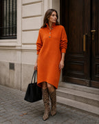 Woman wearing an orange knit midi jumper dress with button-up collar, styled with leopard print knee-high boots and a black tote.