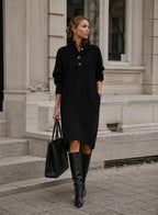 Front view of a black knit midi jumper dress with ribbed button collar, paired with knee-high black leather boots and a tote bag.