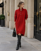Side angle of a red knit midi jumper dress with long sleeves and high-low hem, styled with black knee-high boots on a city street.