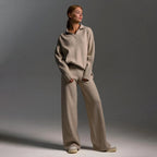 Woman in sand coloured oversized polo jumper and wide leg knit trousers with grey trainers, full front view