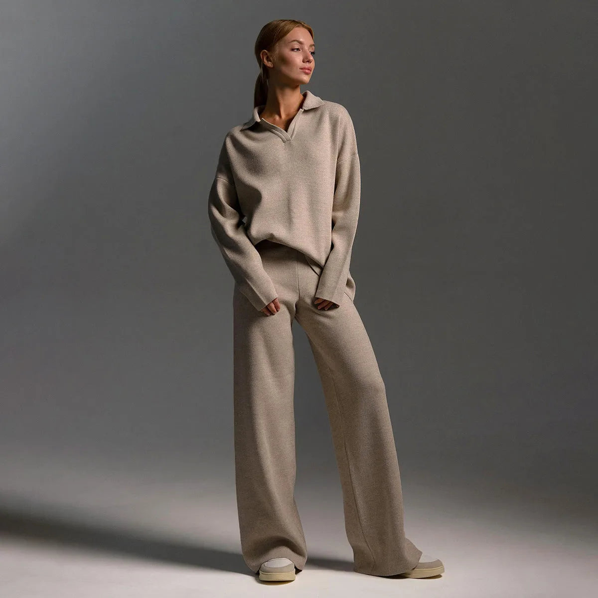 Detail of the wide leg knit trouser hem resting over grey and cream trainers