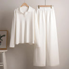 Cream polo jumper and wide leg knit trousers set hanging on wooden hangers against a plain wall