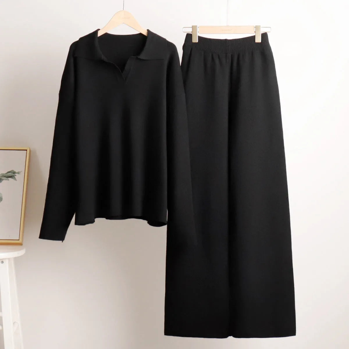 Black polo jumper and wide leg knit trousers set displayed hanging side by side on hangers