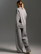 Back view of model wearing the grey oversized polo jumper and wide leg knit trousers with trainers