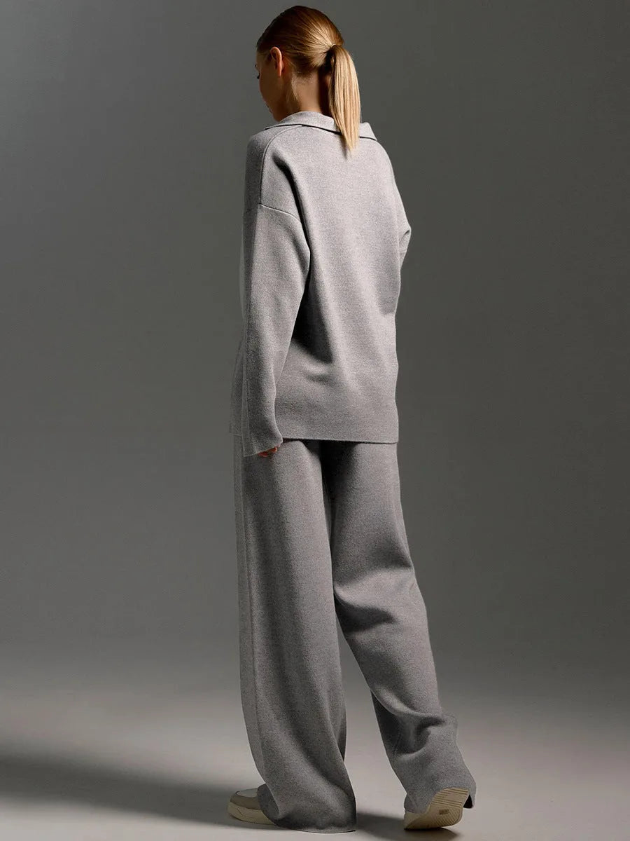 Back view of model wearing the grey oversized polo jumper and wide leg knit trousers with trainers