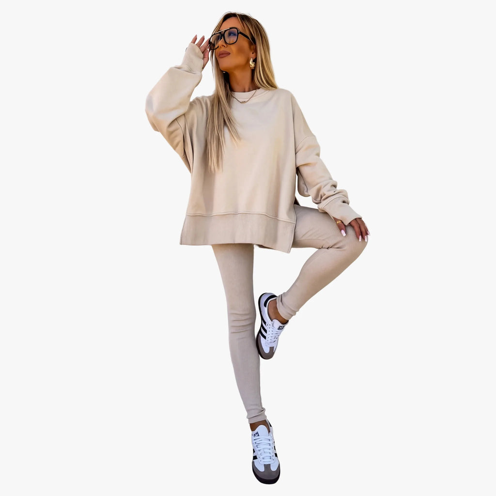 Woman in an oversized beige knit sweatshirt and ribbed leggings with white and black trainers, mid-pose