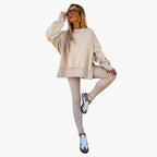 Woman in an oversized beige knit sweatshirt and ribbed leggings with white and black trainers, mid-pose