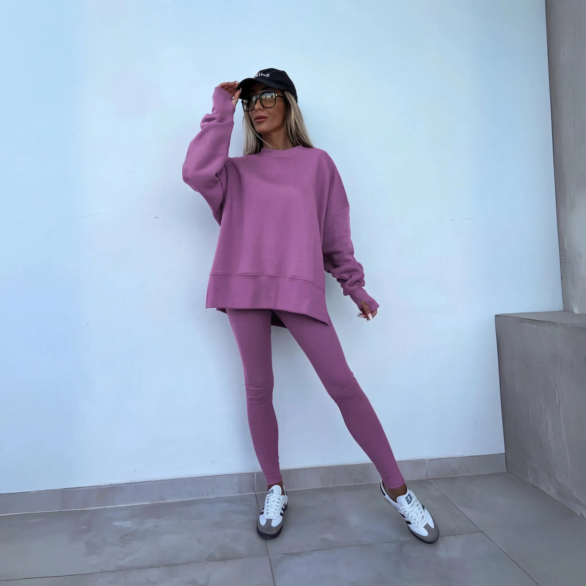 Purple oversized crewneck sweatshirt and matching leggings worn with a cap and white trainers