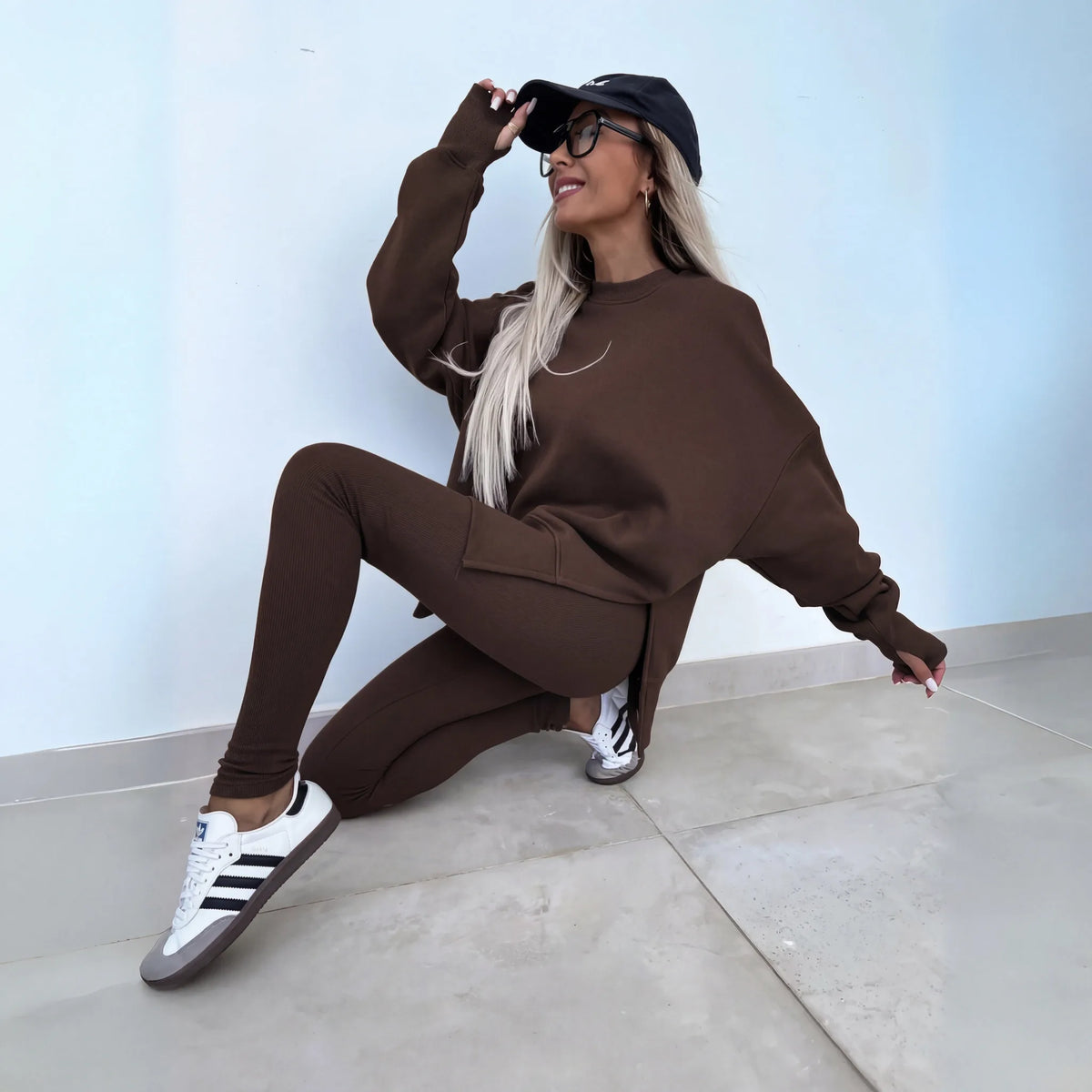 Chocolate brown ribbed leggings and matching oversized sweatshirt shown in a seated pose with trainers