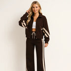 Woman wearing a brown zip-up tracksuit jacket with cream diagonal stripes and matching wide-leg brown joggers