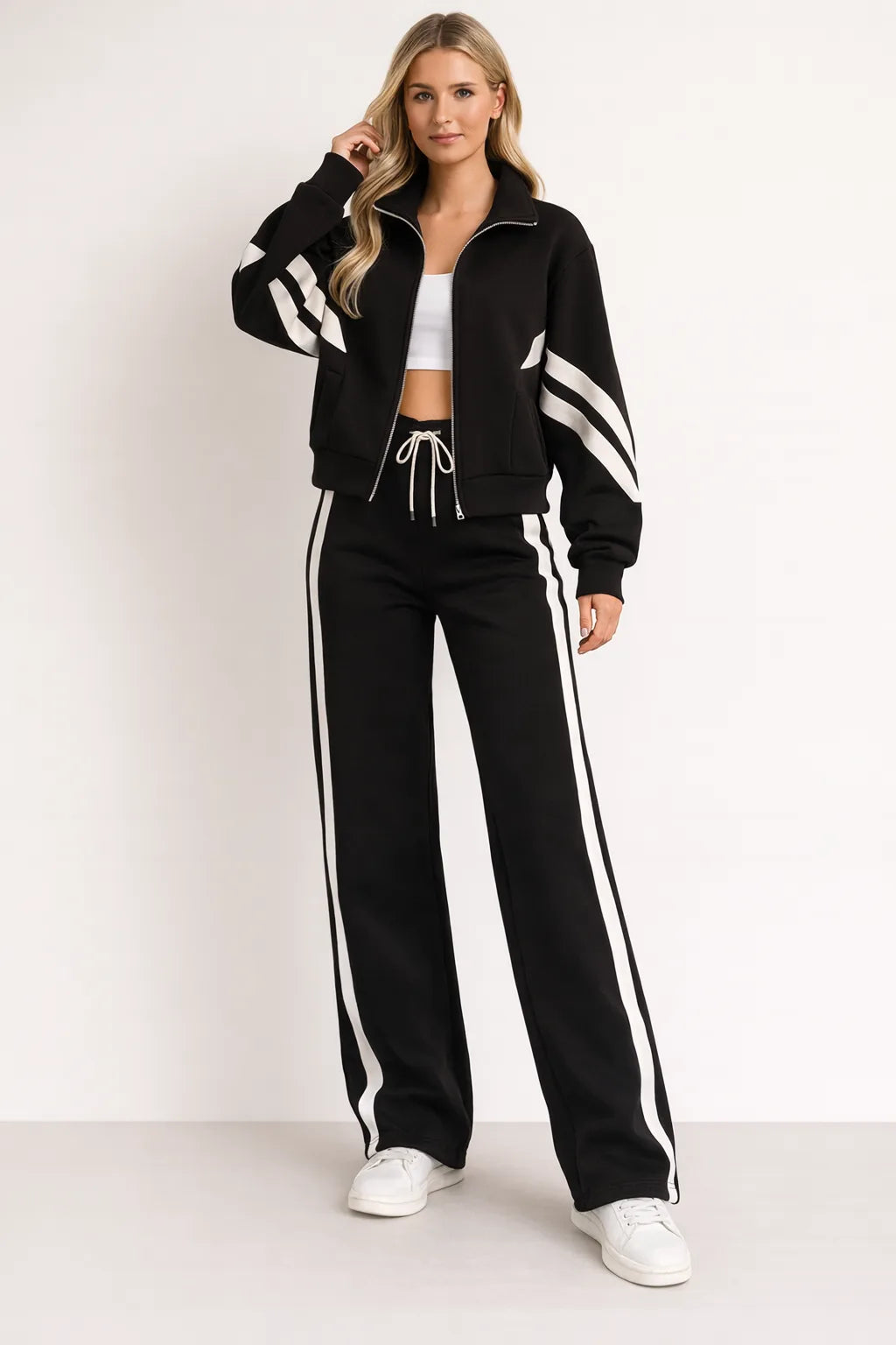 Full-length view of a black zip-up tracksuit jacket with white sleeve stripes worn with white-striped wide-leg joggers and trainers