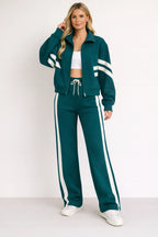 Woman modelling a teal zip-up tracksuit jacket with cream sleeve stripes paired with matching wide-leg teal joggers