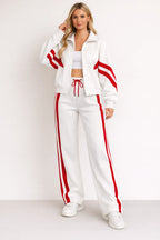 White zip-up tracksuit jacket with red sleeve stripes styled with white wide-leg joggers featuring red side stripes and trainers