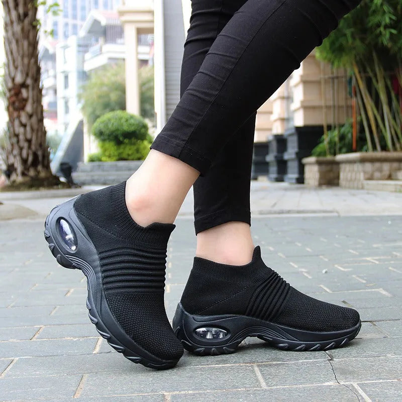 Side view of black knitted slip-on trainers with air-cushion sole worn with black leggings on a city street