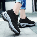 Close-up of black and grey sock-style trainers showing the ribbed knit upper and visible air bubble heel