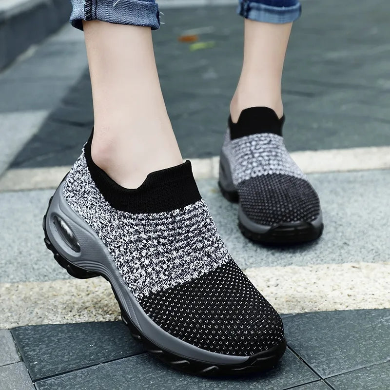 Hand holding a blue and black knitted sock trainer, showing the ribbed texture and grey air-cushion sole