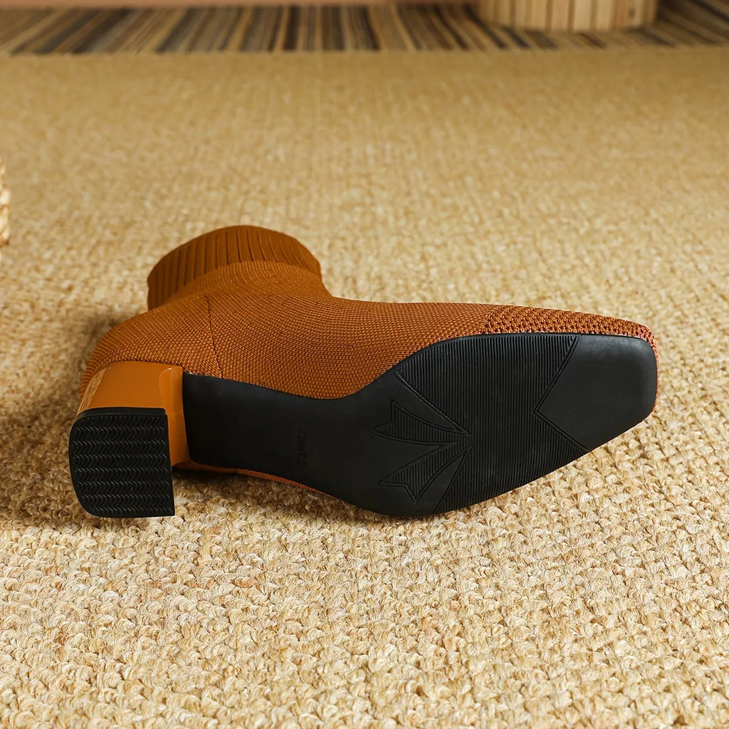 Underside view of a rust orange knit boot showing the textured rubber sole and block heel