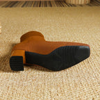 Underside view of a rust orange knit boot showing the textured rubber sole and block heel