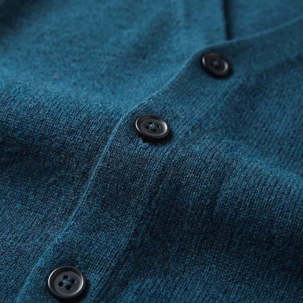 Close-up view of the button placket and ribbed side seam on a teal knitted waistcoat