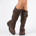 Front view of model wearing brown lace-up knee-high boots with buckle straps and antique eyelets