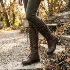 Close-up of model wearing brown lace-up knee-high boots outdoors on a stone step in autumn