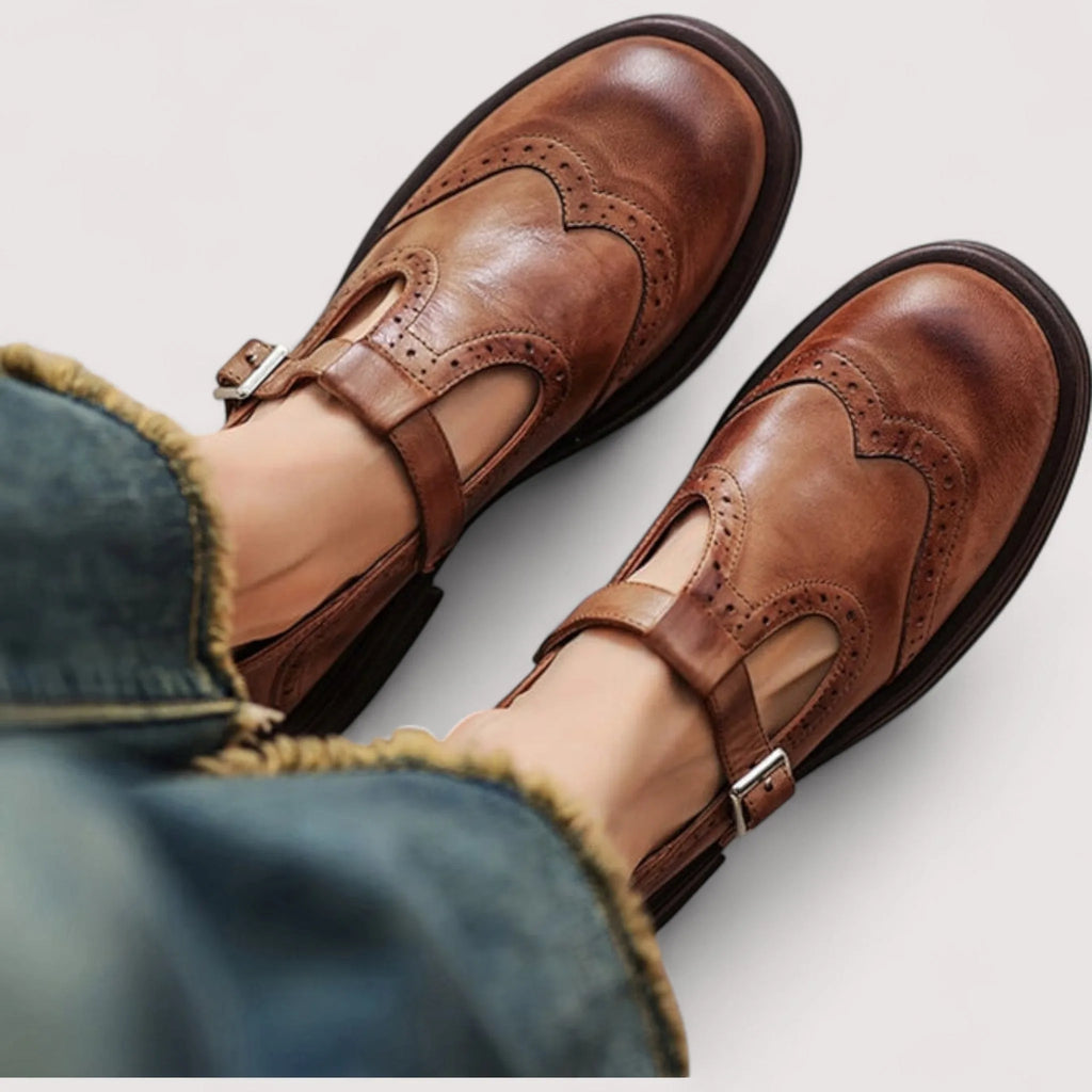 Close-up from above of tan brown leather Mary Jane shoes with brogue wingtip detailing worn with cropped denim jeans