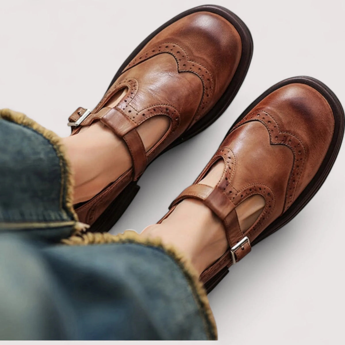 Close-up from above of tan brown leather Mary Jane shoes with brogue wingtip detailing worn with cropped denim jeans