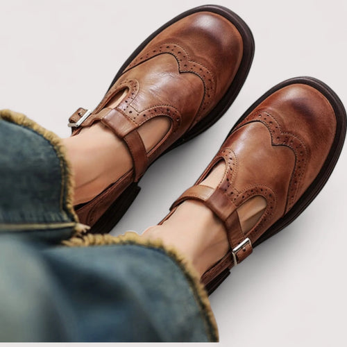 Close-up top-down view of tan brown leather Mary Jane shoes with brogue wingtip detailing worn on bare feet