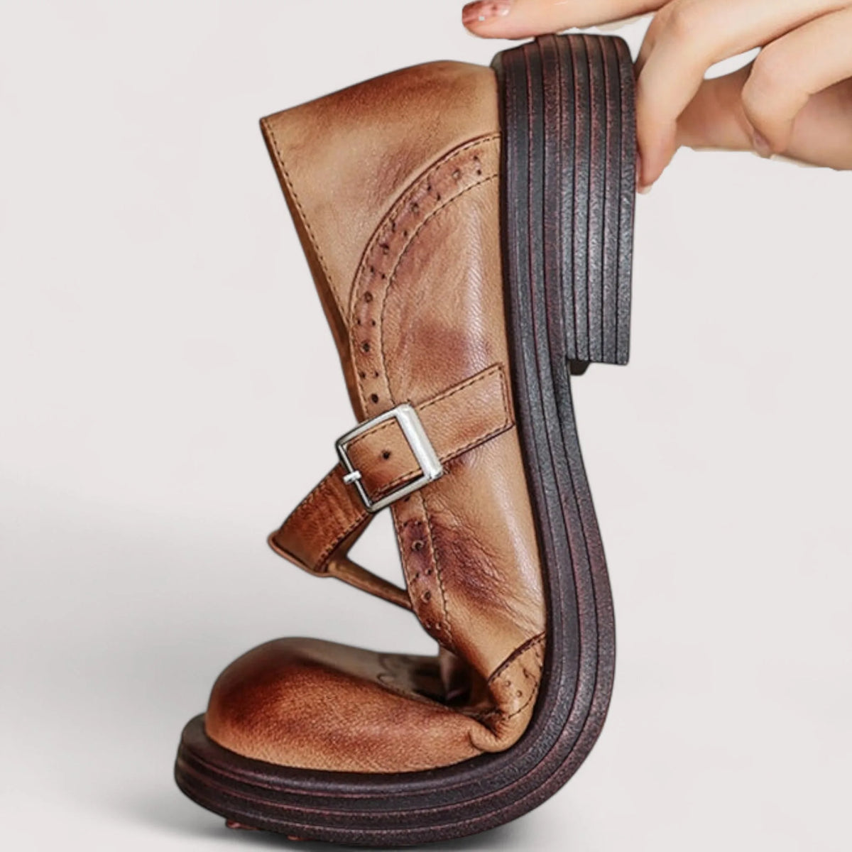 Side profile of a tan leather Mary Jane shoe held up to show the flexible sole and stitched heel construction