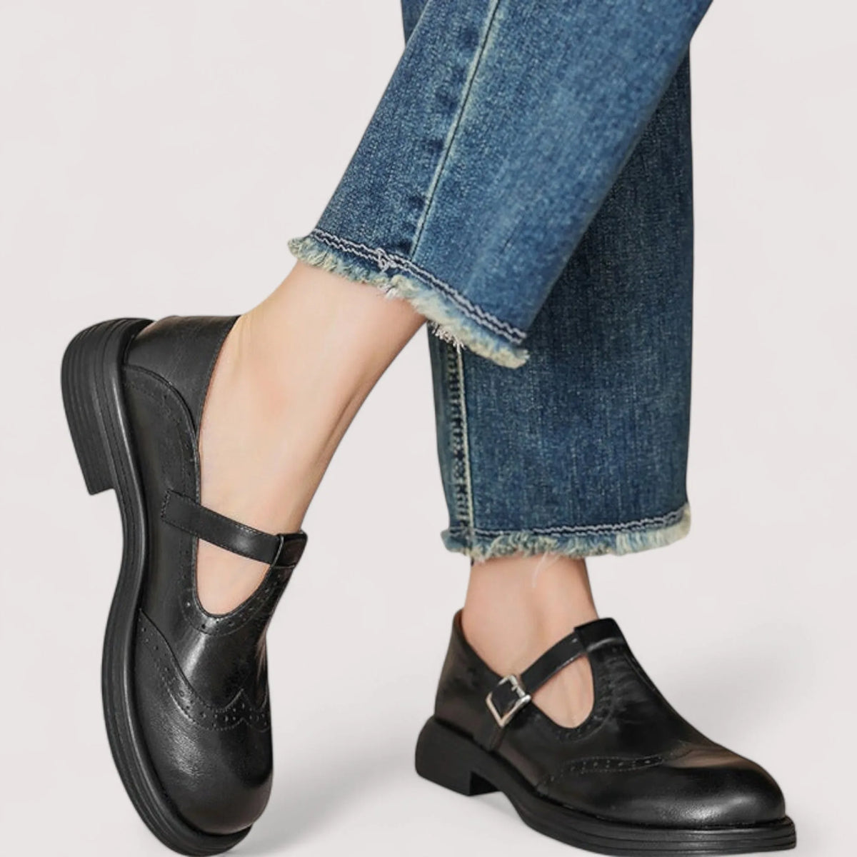 Black leather Mary Jane shoes with T-strap buckle worn on crossed ankles with frayed denim hem
