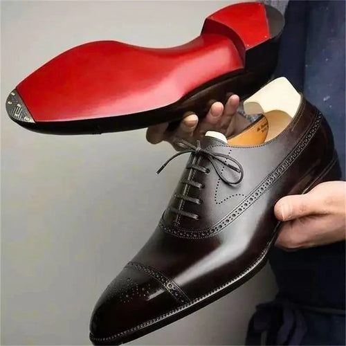 Sole view of a dark brown leather brogue oxford shoe held up, showing a vivid red leather sole and brogue toe cap detailing