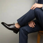 Man seated wearing dark brown brogue oxford shoes with navy pinstripe tailored trousers, side view of the shoe on foot