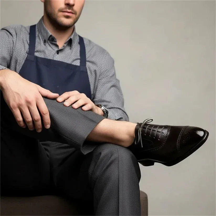 Man seated wearing dark brown brogue oxford shoes with grey trousers and a checked shirt, close crop on the footwear