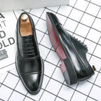 Pair of glossy black brogue oxford shoes with wooden shoe trees, one shoe turned to show the burgundy sole