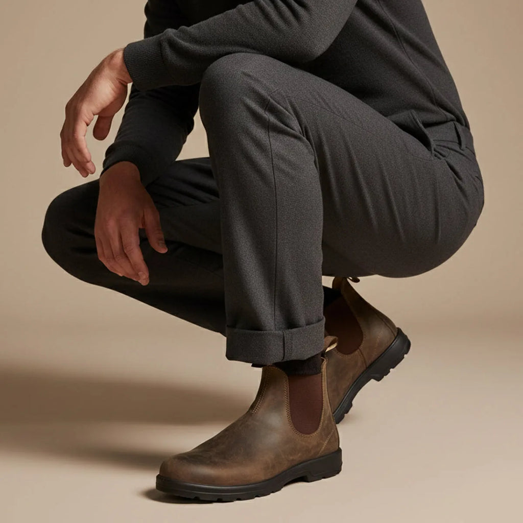Man crouching wearing rustic brown Chelsea boots with rolled grey joggers, close-up on footwear