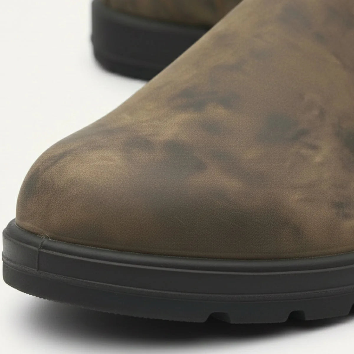 Detail shot of the rounded toe and tread sole on a distressed brown leather Chelsea boot