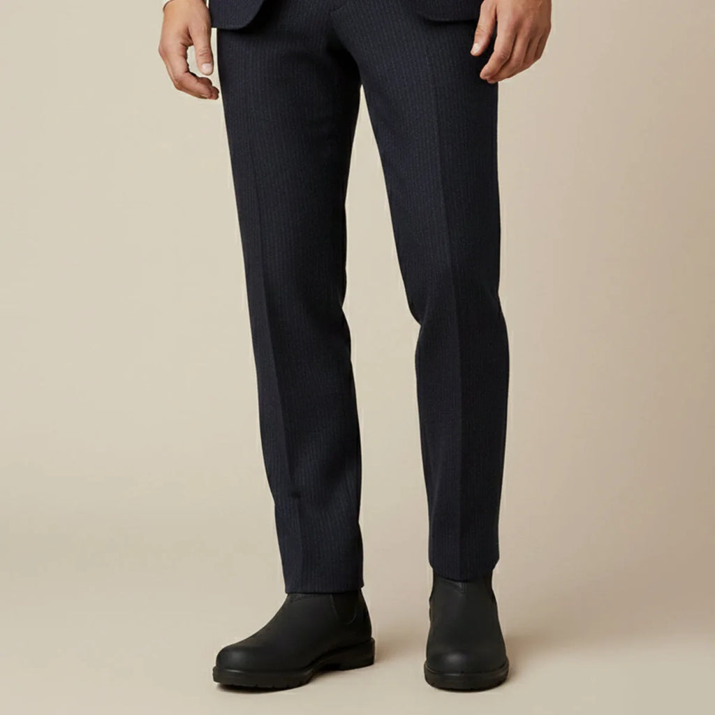 Close-up of a man's legs in navy pinstripe trousers rolled above black Chelsea boots