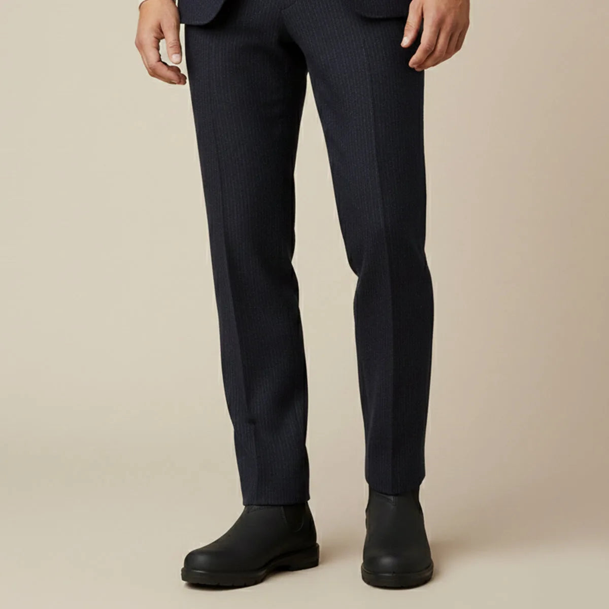 Close-up of a man's legs in navy pinstripe trousers rolled above black Chelsea boots