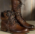 Close-up of dark brown leather boots with a fold-down cuff, checked lining and brass-tone press studs