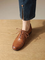 Close-up front angle of a single tan leather oxford shoe showing cap-toe seam and dark brown sole