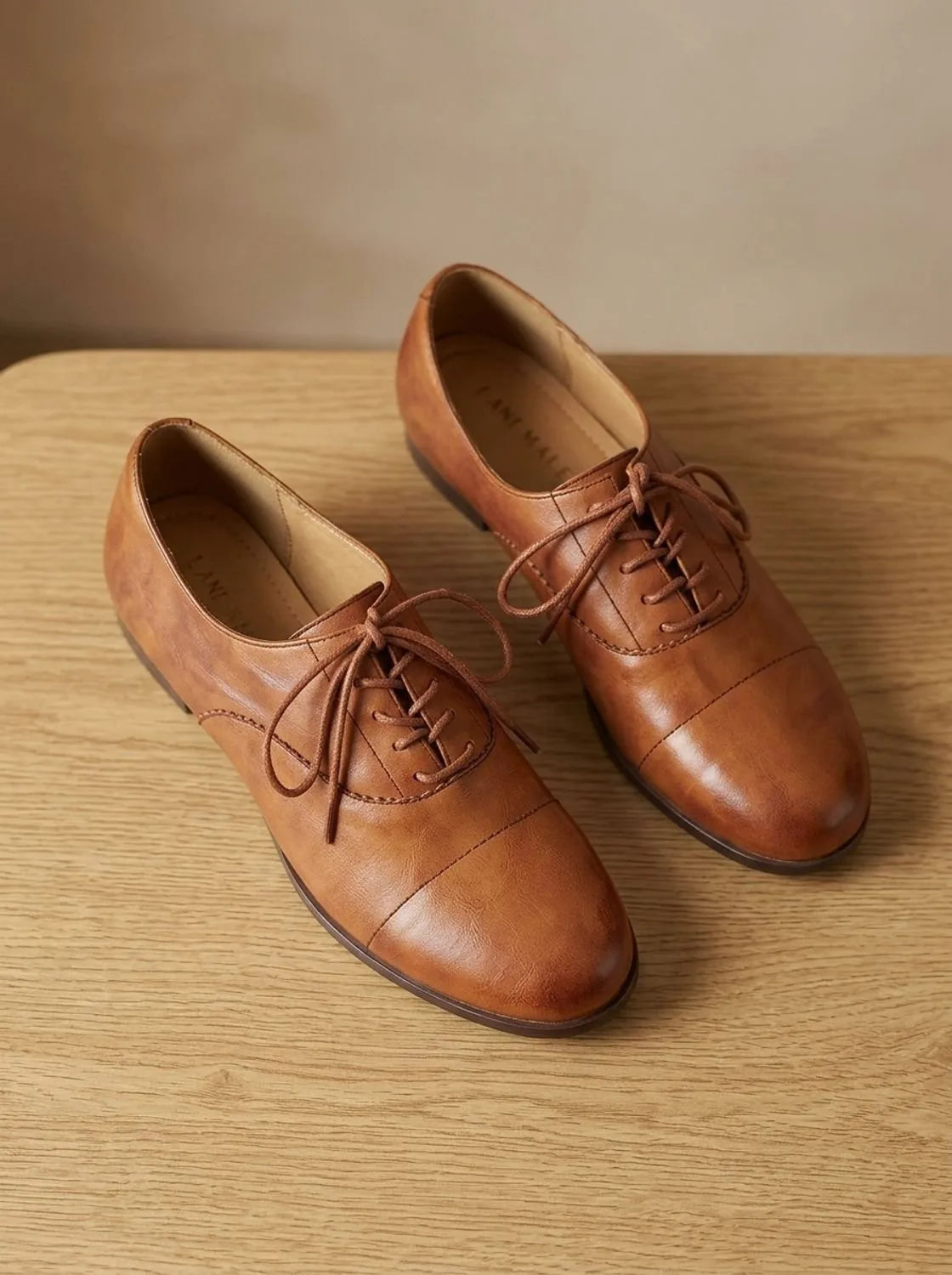 Top-down close-up of a tan leather oxford shoe on foot with laces tied, denim trouser hem with heart button detail
