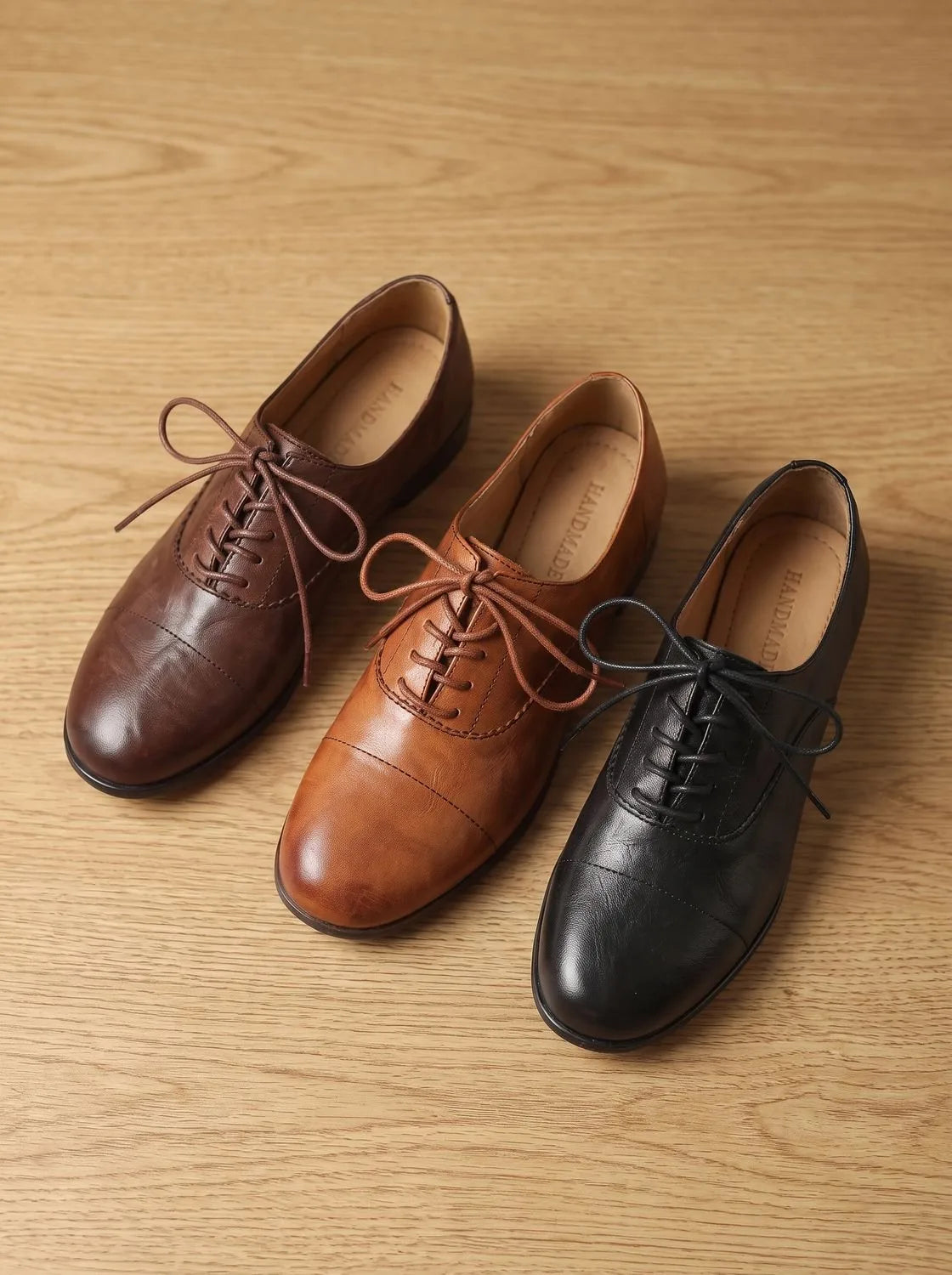 Close-up front view of crossed feet in tan leather oxford shoes, denim hem and beige wall in background
