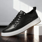Side profile of black leather lace-up trainer with white midsole and gum outsole against a bright studio backdrop