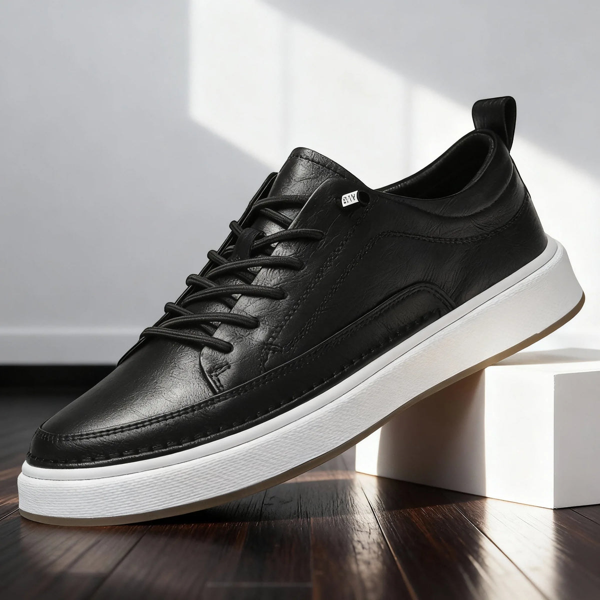 Side profile of black leather lace-up trainer with white midsole and gum outsole against a bright studio backdrop