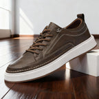 Side view of khaki brown leather trainer showing contrast stitching and white cupsole, resting against a white block