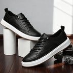 Pair of black leather trainers with lace detail and gum soles styled beside a vintage camera on wooden flooring
