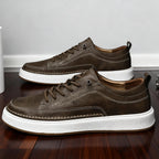 Side-by-side pair of khaki brown leather trainers showing stitched toe panel and white sole on wood flooring