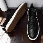Overhead view of one black trainer on its side revealing gum tread pattern next to a second shoe shown upright